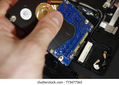 engineer changes hard drive in old laptop close-up. Engineer's hands with hdd on background of disassembled laptop. Repairs electronics