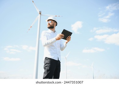 Engineer is checking energy production on wind turbine. Worker in windmills park.