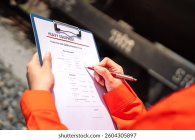An engineer is checking heavy machine checklist form during inspecting condition, with blurred background of train and railway. Transportation industrial working with safety practice, close-up. 