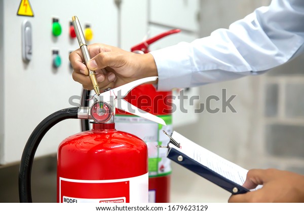 Engineer are checking and inspection a red fire\
extinguishers in the fire control room for safety prevention and\
fire training.