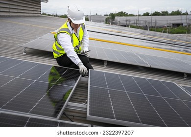 Engineer checking installation of solar panels installed on factory roof, checking installation of solar panels. Asian engineer records inspection data on tablet, supervising solar panel installation.