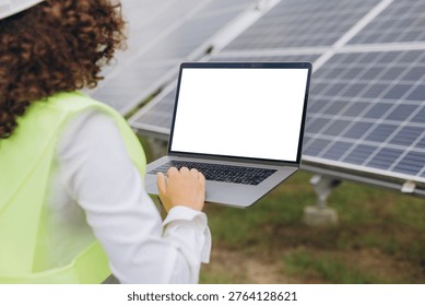 Engineer checking solar panel performance on laptop with blank screen, monitoring renewable energy system