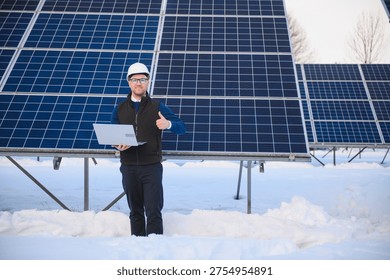 Engineer checking solar panels with a laptop, giving a thumbs up. Promoting renewable energy in a snowy winter landscape