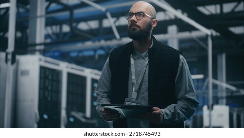 Engineer Checking System Metrics on Digital Tablet. Bearded IT Engineer in Dark Vest and Glasses Monitors System Metrics on Digital Tablet Amidst Server Racks. Cloud Auditing, and Technical Analysis.