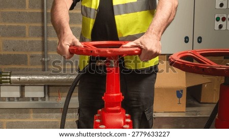 Engineer checking water supply pump on red valve for sprinkler fire protection system. Close up of engineers hands working on a sprinkler fire suppression system. Industrial fire prevention equipment.