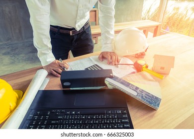 Engineer concept : Architect working on blueprint.engineer inspective in workplace , laptop ,calculator, house model, blueprints,helmet. Vintage filter effect