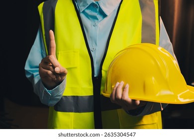 Engineer concept. Construction Worker in Safety Vest Holding Hard Hat with One Finger Raised Indicating Caution or Warning Sign.