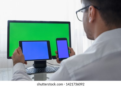 Engineer, Constructor, Designer in Glasses Working on a Personal Computer with a Green Screen on Monitor which has Chroma Key Great for Mockup Template. Male Using Smartphone or Tablet with Blue - Powered by Shutterstock