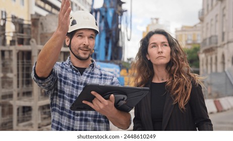 Engineer constructor discuss build plan with investor woman. Builder guy show construction site project tablet pad. Worker tell blueprint client. Man work city street. Customer look new house scheme.