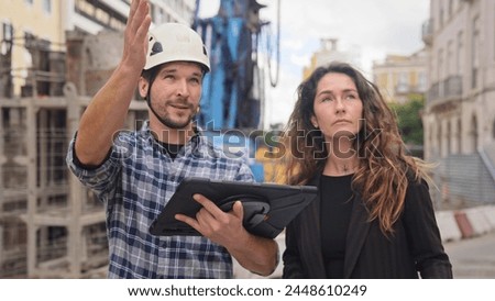 Engineer constructor discuss build plan with investor woman. Builder guy show construction site project tablet pad. Worker tell blueprint client. Man work city street. Customer look new house scheme.