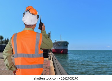 Engineer And Crane. Smiling Dock Worker Holding Radio Walkie Talkie And Ship Background