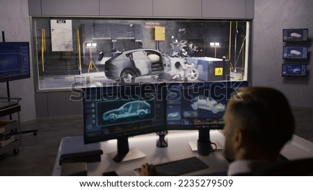 An engineer in a crash test lab uses a car crash test system to simulate a traffic accident, to obtain the safety parameters of an eco-friendly cutting edge electric vehicle being developed.