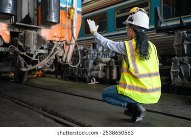 An engineer crouched by a train wheelset, analyzing data on a laptop, within the industrial surroundings of a train maintenance depot.