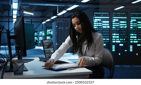 Engineer in data center installing software on computer, helping maintain network, troubleshooting arising issues. IT expert in server room establishing performance benchmarks, camera B - Powered by Shutterstock