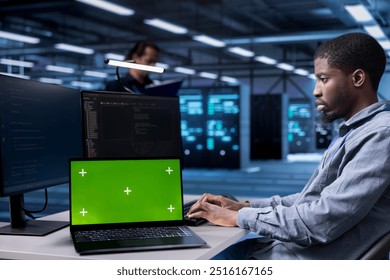 Engineer in data center running system diagnostic tests using isolated screen laptop. African american man in server farm deploying error checking utilities on mockup notebook to repair network issues