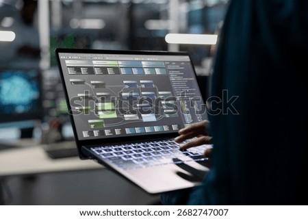 Engineer in data center uses AI technology on laptop for machine learning workloads. Server hub facility employee using artificial intelligence on notebook to perform demanding computing tasks