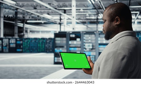 Engineer in data center using green screen tablet to develop disaster recovery plans. IT expert in server farm testing failover scenarios on mockup device, protecting data during disruptions, camera A