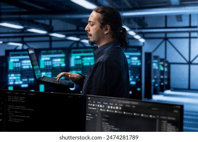 Engineer in data center using laptop to find firewall misconfigurations affecting rackmounts performance. Worker in server farm checking systems bottlenecks leading to sluggish data transfer rates