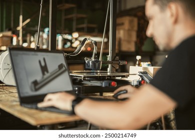 An engineer designs a 3D element on a laptop that is being printed on a 3D printer in a sunlit workshop. The image captures the creative process