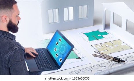 Engineer Develops A Smart Home System. He Thinks About Arrangement Of Smart Furniture. Architect Holds A Laptop In His Hands. Software Engineer Next To Architectural Drawings. Setting Up A Smart Home