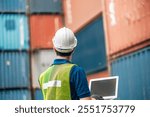 Engineer dock worker in protective safety jumpsuit uniform and with hardhat and use laptop computer at cargo container shipping warehouse. transportation import,export logistic industrial