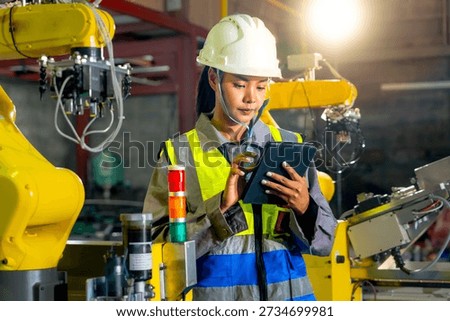 The engineer examines data on a tablet near the robot arm regarding industrial automated manufacturing processes technological safety devices and factory workflows.

