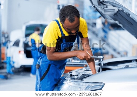 Engineer expertly examines car wheels using advanced mechanical tools, ensuring optimal automotive performance and safety. BIPOC trained garage employee conducts annual vehicle checkup