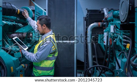 Engineer of factory using tablet controlling program to automatic generator machinery on the engine room, inspecting the generator with tablet.
