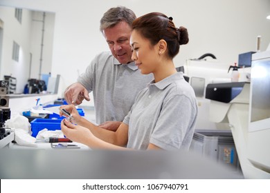 Engineer And Female Apprentice Measuring Components In Factory