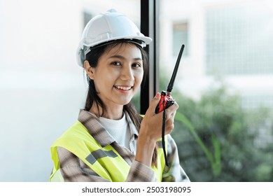 Engineer Female Construction Worker Smiling and Holding Walkie-Talkie in Safety Gear at Construction Site - Powered by Shutterstock