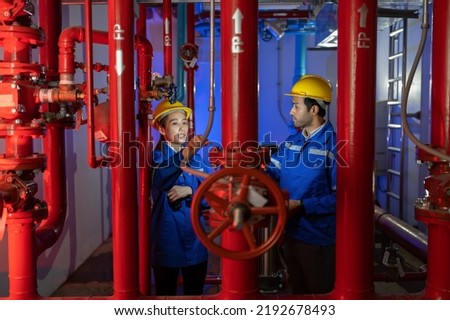 An engineer in the fire protection pump room talking with walkie talkie checking and operate trouble shooting defective spray nozzle head valve at the red pipeline
