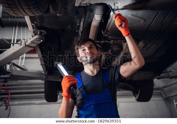 Engineer fixing car suspension and using a\
small flashlight