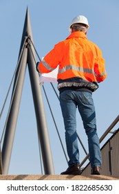 Engineer or foreman with hard hat and protective workwear reading a plan in front of industrial background - selective focus