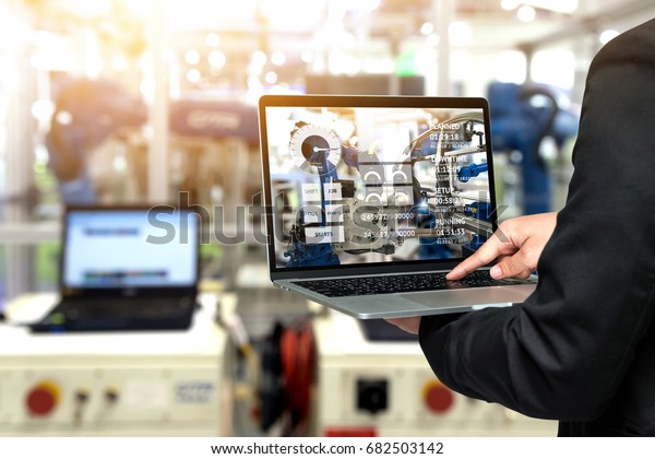 Engineer hand using laptop with machine real\
time monitoring system software. Blur automation robot arm machine\
in smart factory Industry 4th iot , digital manufacturing operation\
technology concept.