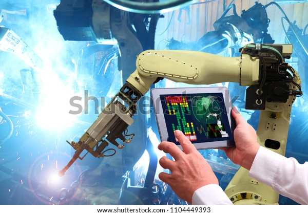 Engineer hand using tablet with machine real time\
monitoring system software.digital manufacturing operation.\
Automation robot arm machine in smart factory automotive industrial\
, Industry 4.0 concept