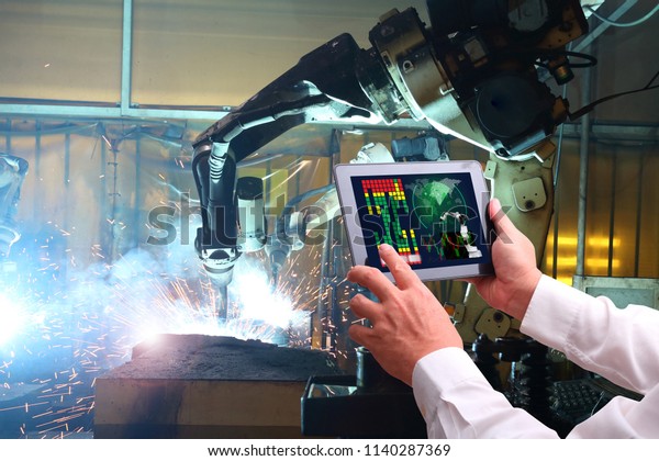 Engineer hand using tablet with machine real time\
monitoring system software.digital manufacturing operation.\
Automation robot arm machine in smart factory automotive industrial\
, Industry 4.0 concept