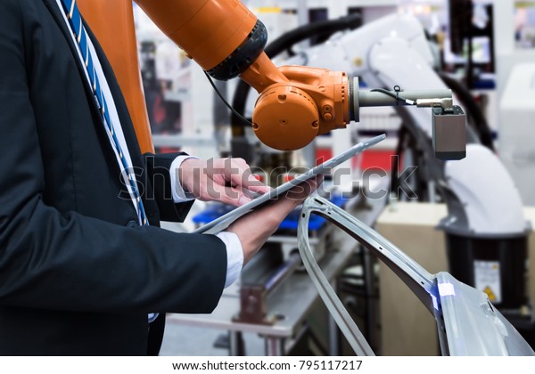 Engineer hand using tablet with machine real\
time monitoring system software. Automation robot arm machine in\
smart factory automotive industrial Industry 4th iot , digital\
manufacturing\
operation.