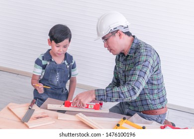 Engineer Handy Man Father Is Teaching His Boy To Work On Construction Woodwork Tools. Son Is Learning Wood Craft From Dad For Family Togetherness Concept