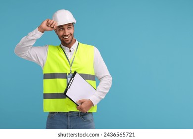 Engineer in hard hat holding clipboard on light blue background, space for text - Powered by Shutterstock