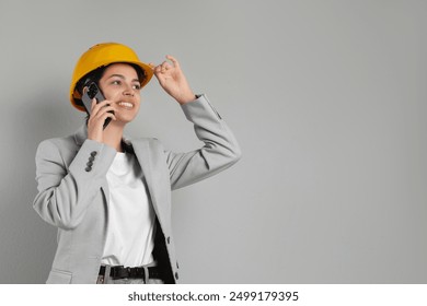 Engineer in hard hat talking on smartphone against grey background, space for text