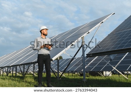 Engineer in hardhat holding tablet, checking solar power plant installation. Concept of green technology and sustainable energy