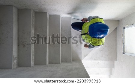 Engineer in hardhat, safety vest and Walkie-Talkie checking house structure while walking up on a stairway. Day time work safety checks. Top View