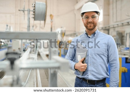 Engineer in hardhat is using a laptop in a heavy industry factory.