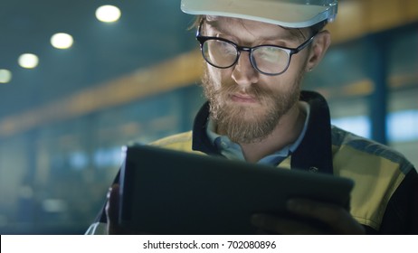 Engineer in hardhat is using a tablet computer in a heavy industry factory.