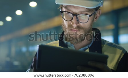 Engineer in hardhat is using a tablet computer in a heavy industry factory.