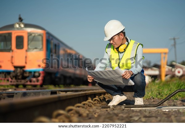 The engineer in a helmet band uniform working\
with a blueprint for the plan, an Engineer working in the railway\
train station.