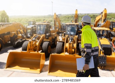 Engineer in a helmet with a digital tablet stands next to construction excavators	