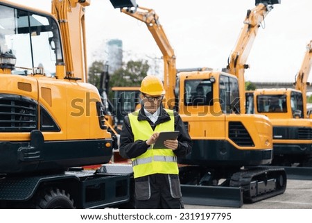 Engineer in a helmet with a digital tablet stands next to construction excavators	