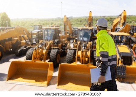 Engineer in a helmet with a digital tablet stands next to construction excavators	