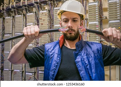 Engineer In A Helmet Will Connect Damaged Internet Backbone Wire. Worker Restores The Connection In The Data Center Server Room. Technician Holds In His Hands The Two Ends Of Torn Telephone Cable. 